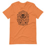 Burnt Orange short sleeve t-shirt with centered skull and cross bones, with small additional artistic accents, surrounded in a circular pattern with "Fortune Favors the Brave". All lettering and imagining is in Black.